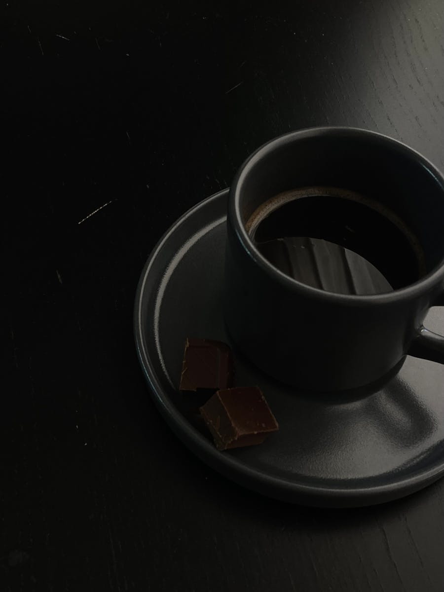 A cup of coffee on a saucer with a piece of chocolate - Roteiro Cafeterias Bogotá