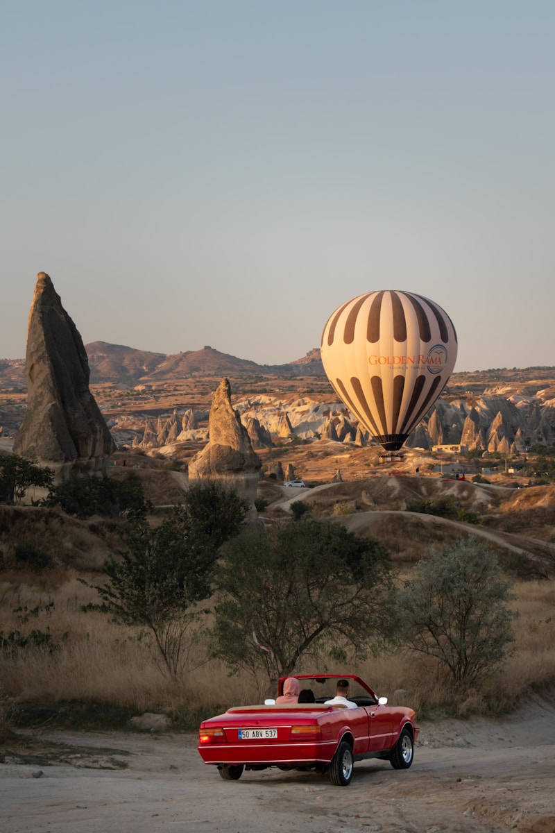 a red convertible car parked in front of a hot air balloon - Passeios de Balão Capadócia