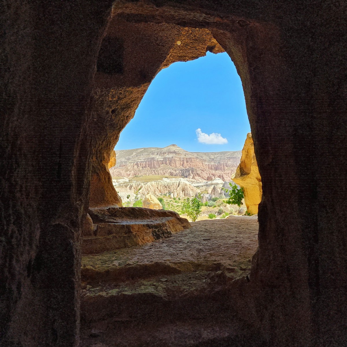 a view through a hole in a rock wall at a city - Passeios de Balão Capadócia